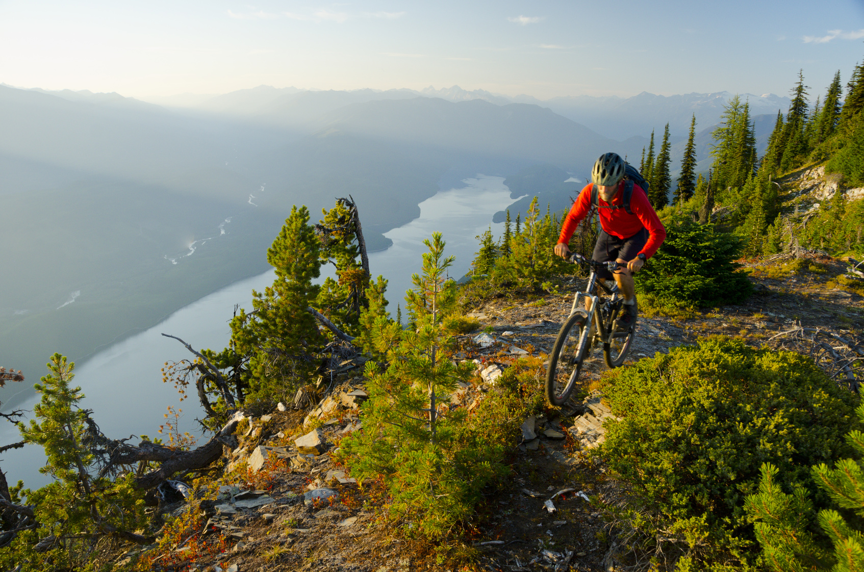 A mountain biker riding high above the valley in the Purcell Mountains — above the treeline, the world shrinks to the trail, the bike, and the distance to the next ridge