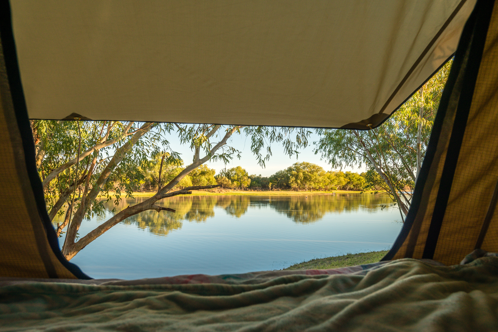 View from a tent doorway over a remote billabong, Northern Territory — the desert night that drops 20°C after sunset, demanding the emergency bivy you almost didn't bring