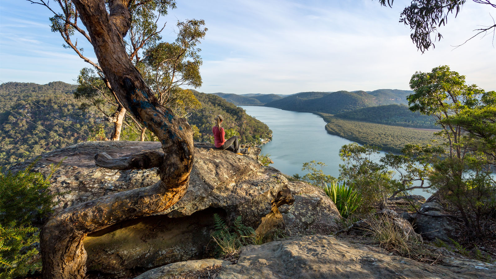 Female sitting on a large rock relaxing in afternoon dappled light in the Australian bushland with river views