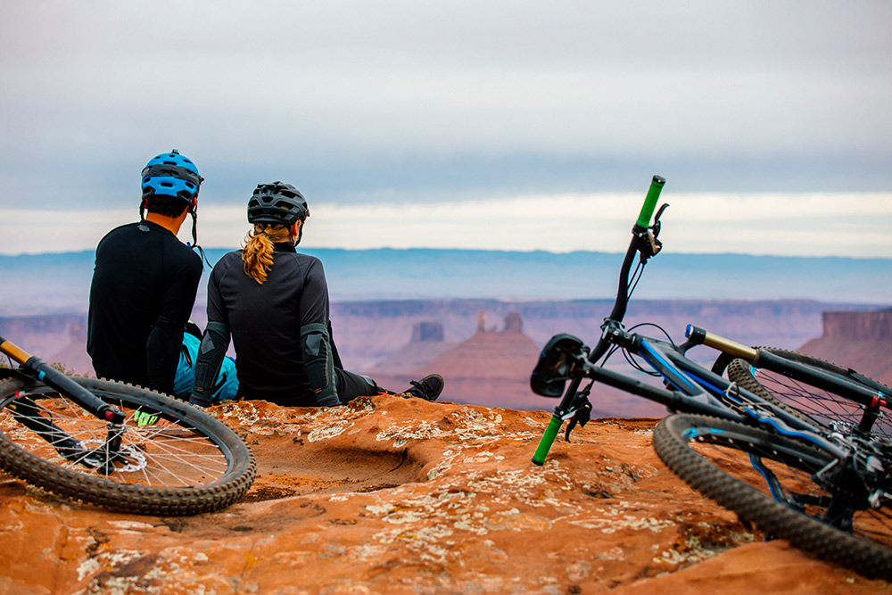 A couple on mountain bikes pausing to take in a panoramic view — every col earns exactly the perspective it cost to reach